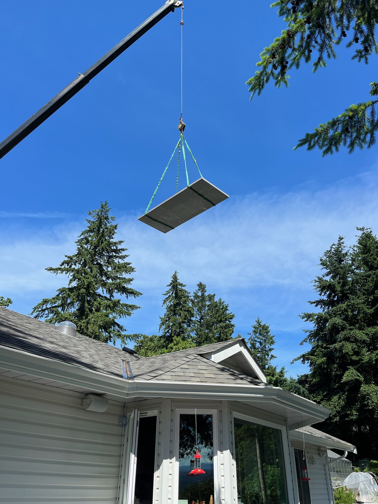 Crane lifting a large stone slab over a house during installation
