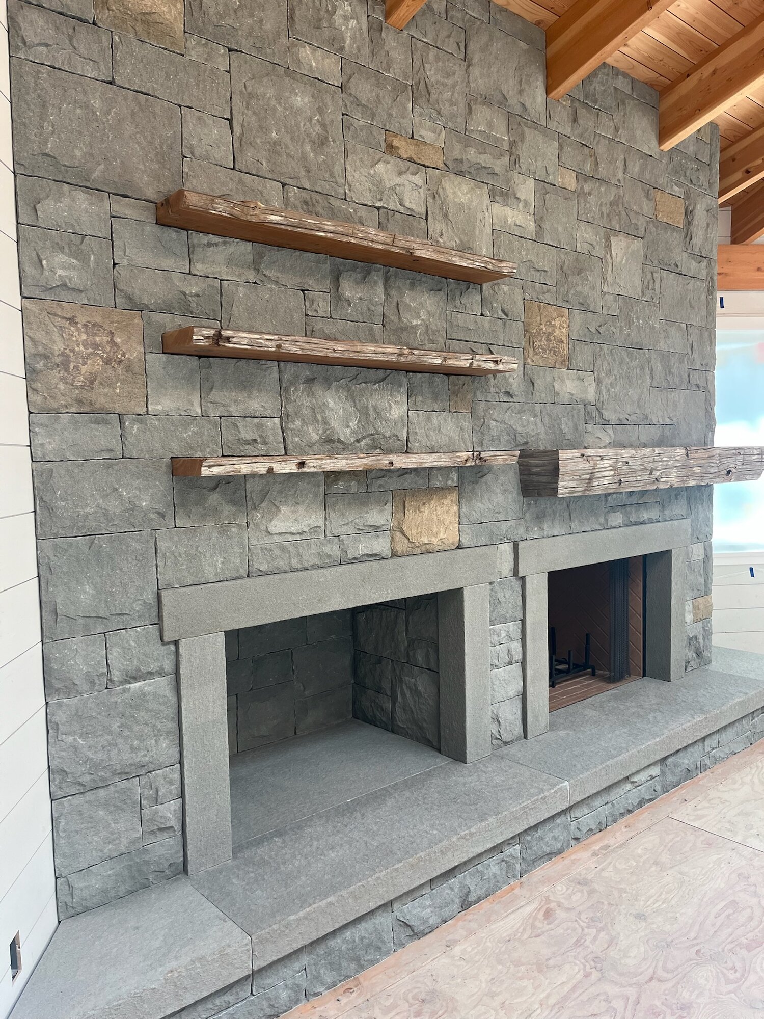 Wide double-firebox stone fireplace wall with three driftwood floating shelves