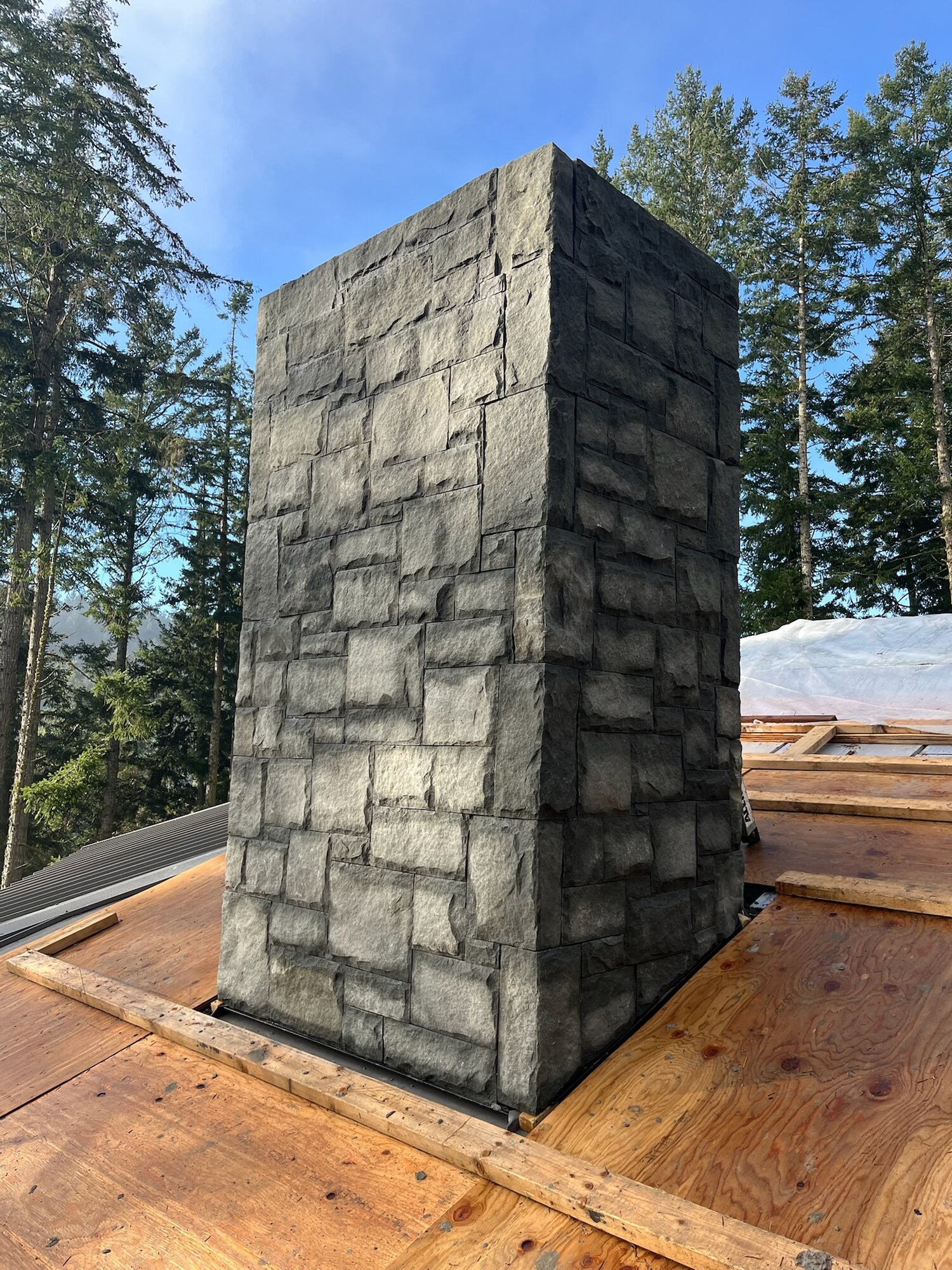 Square grey stone chimney on a rooftop with a mountain and forest backdrop