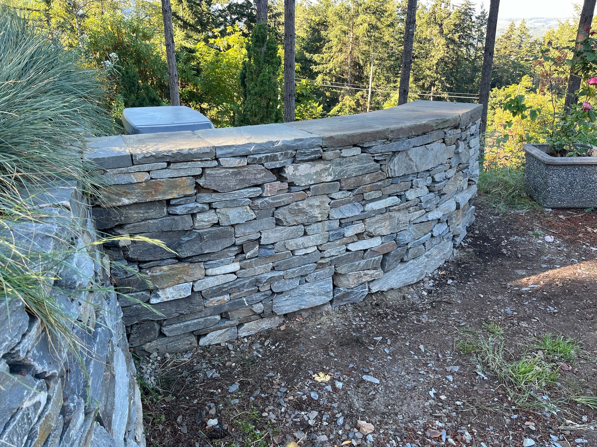 Curved dry-stack retaining wall with flat stone cap in a garden setting