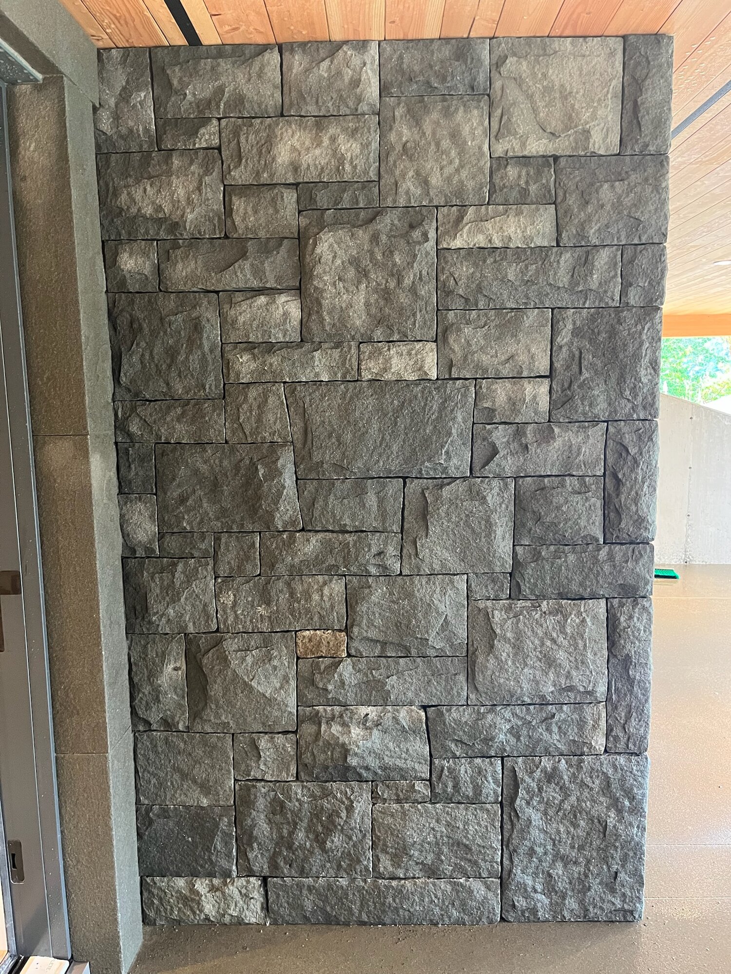 Exterior dark grey rough-face stone wall panel under a covered patio