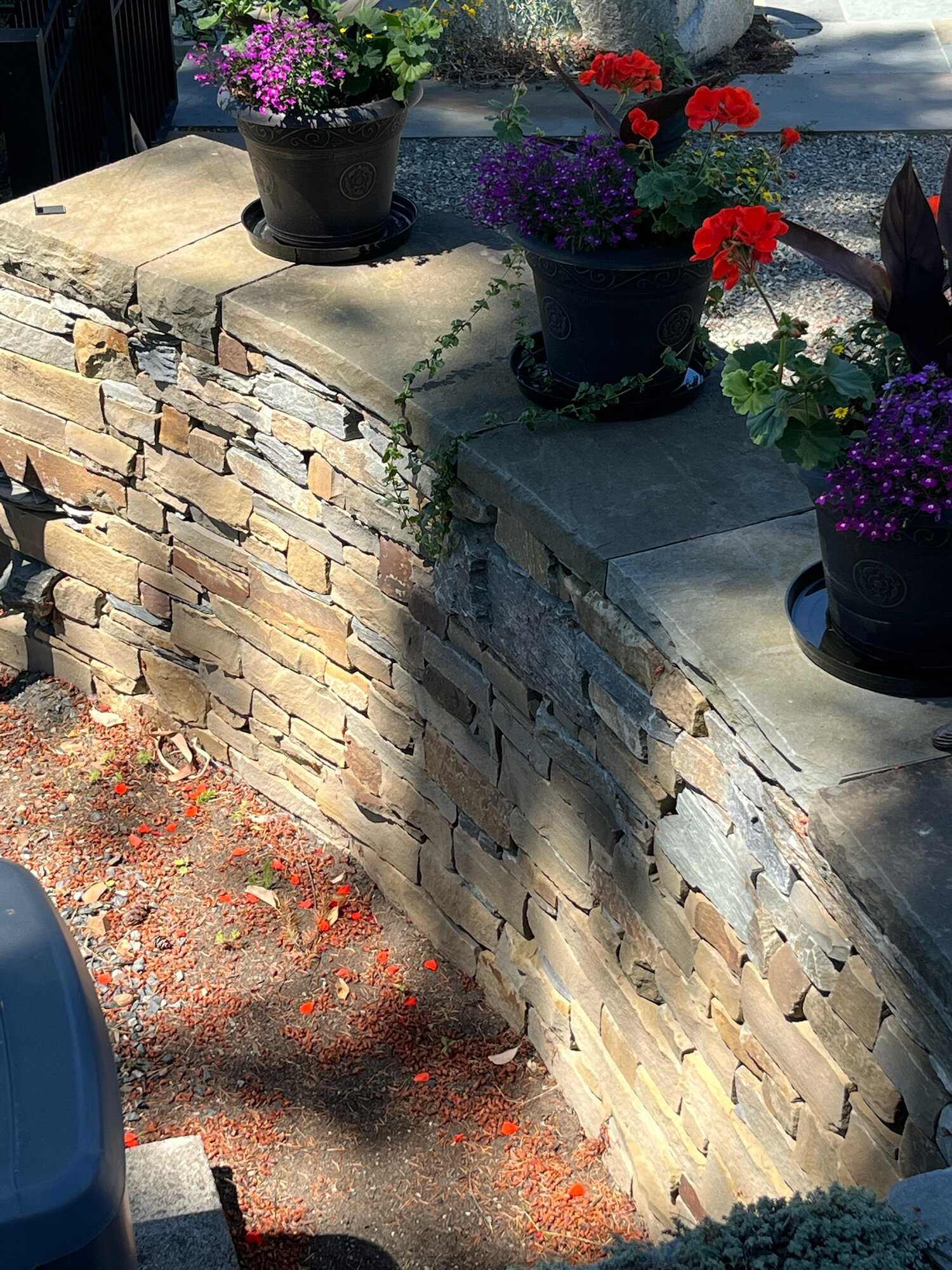 Dry-stack planter wall corner with flower pots on top, warm mixed tones