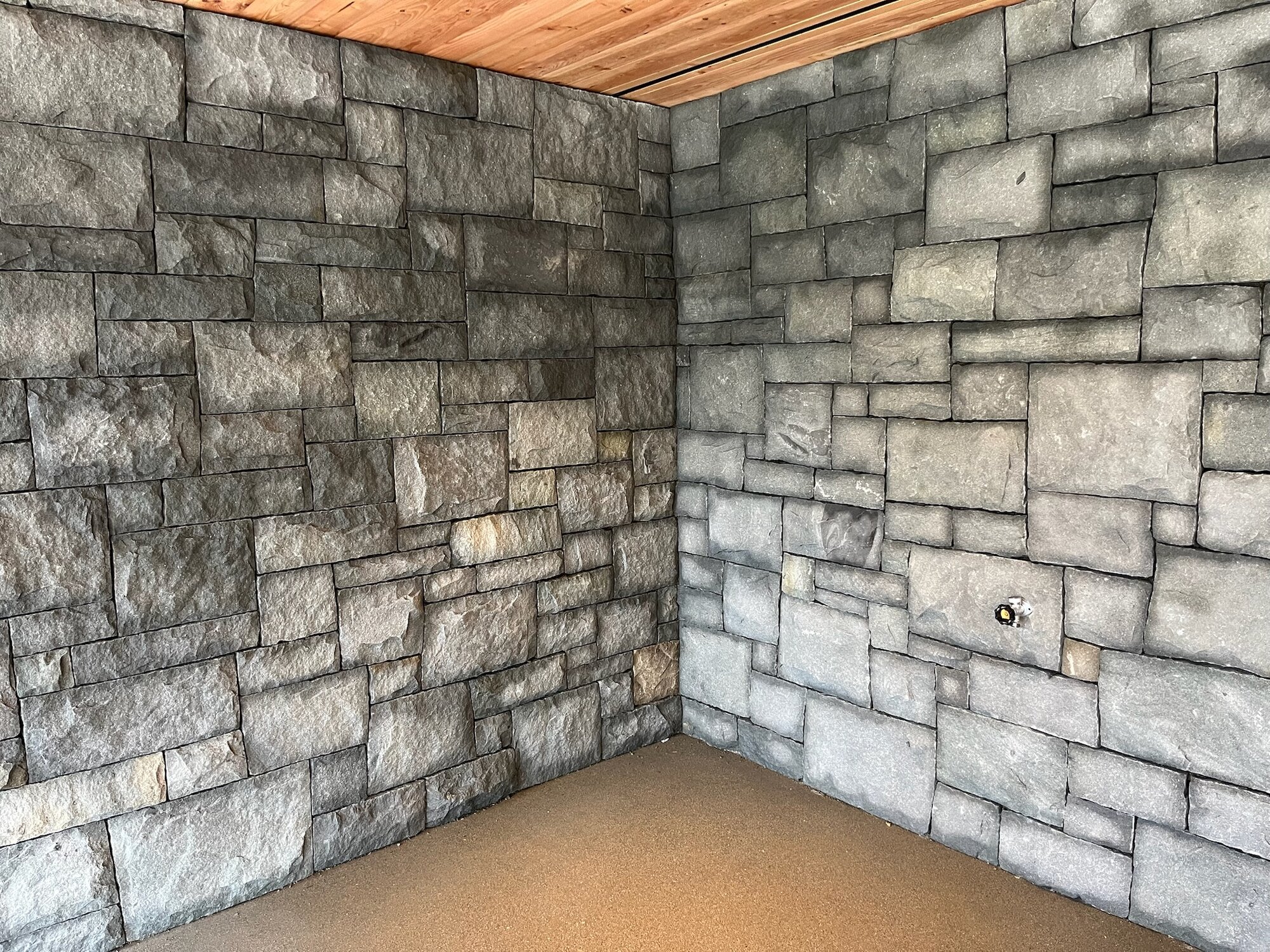 Interior corner of a grey granite stone-clad room with cedar ceiling