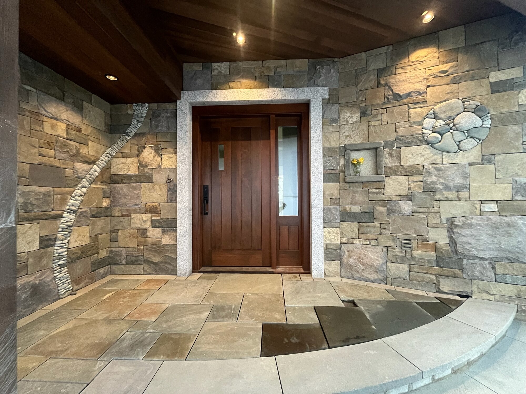 Stone-clad entry foyer with pebble arc, circle inset, wood ceiling, and granite door surround