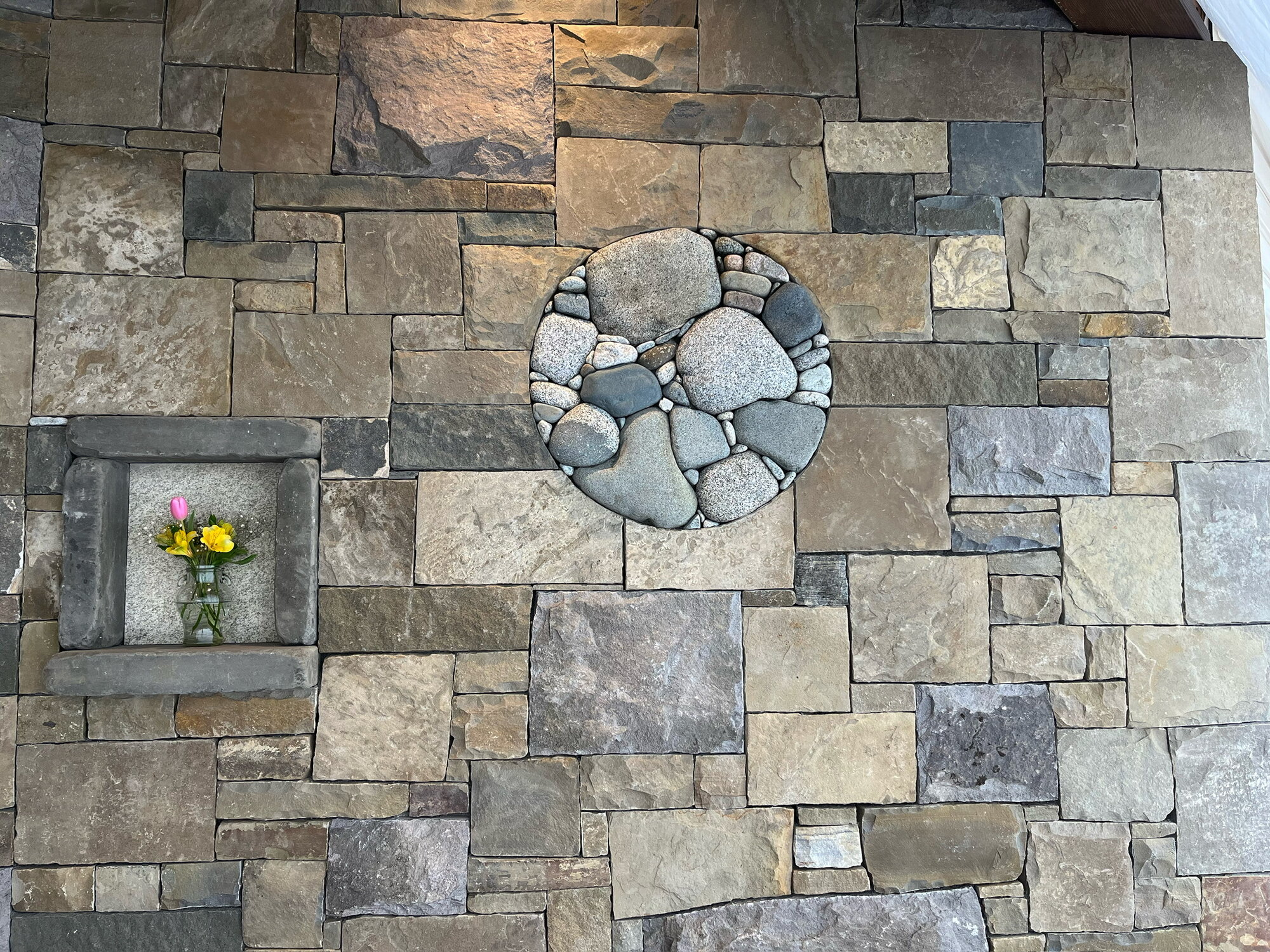 Interior stone wall with a river rock circle inset and stone niche with flowers